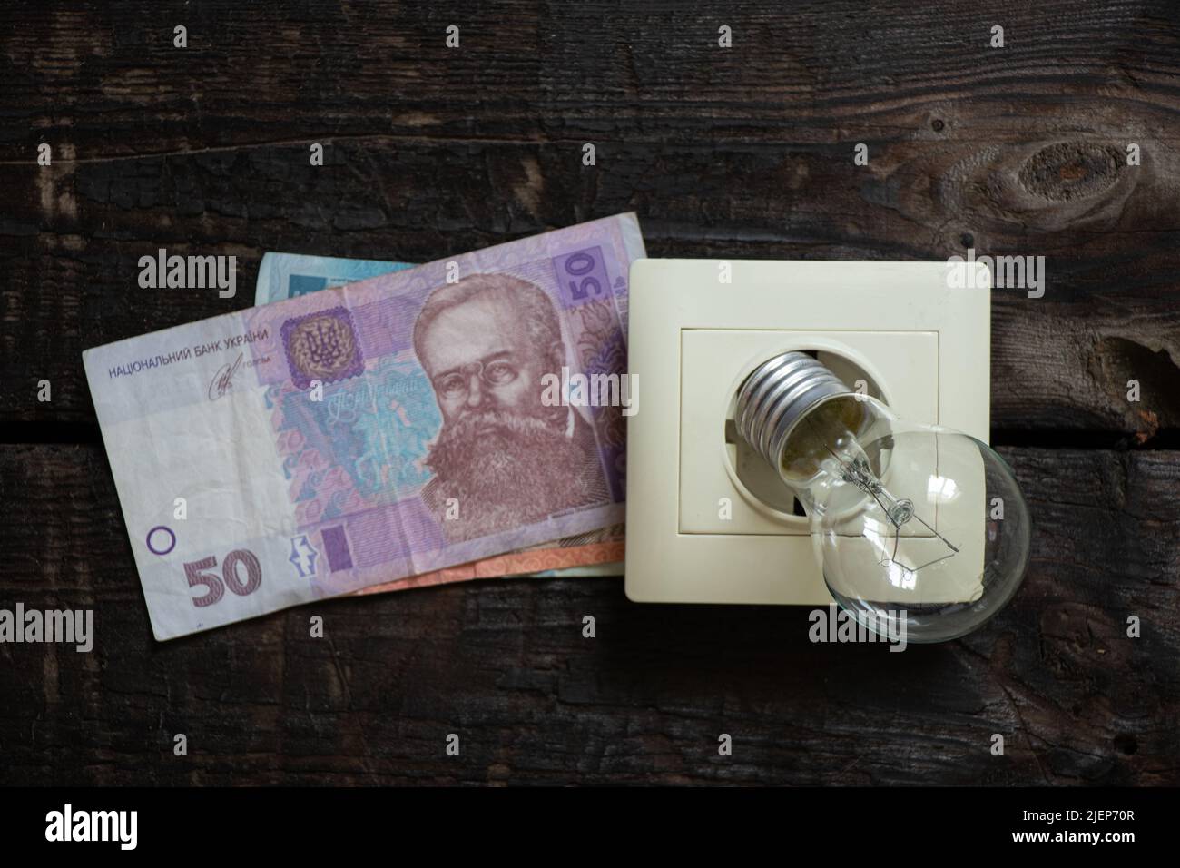 plastic razetkana on an old wooden wall and a light bulb and about 50 hryvnia, rising electricity prices, electricity prices, another rise in price Stock Photo