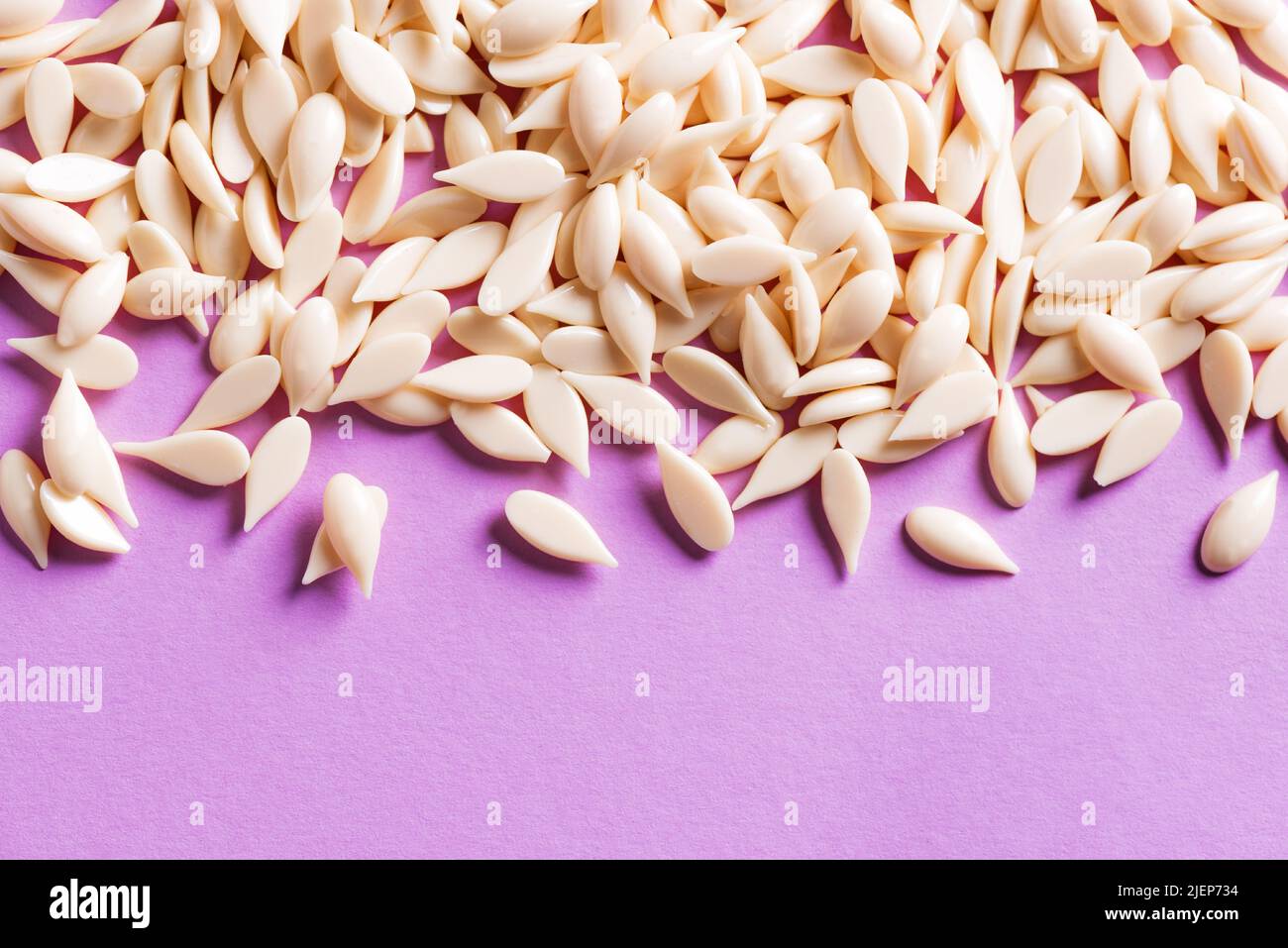 Granular film wax bean granules on purple background, copy space. Natural hair removal, natural beauty concept,  pearl wax. Stock Photo