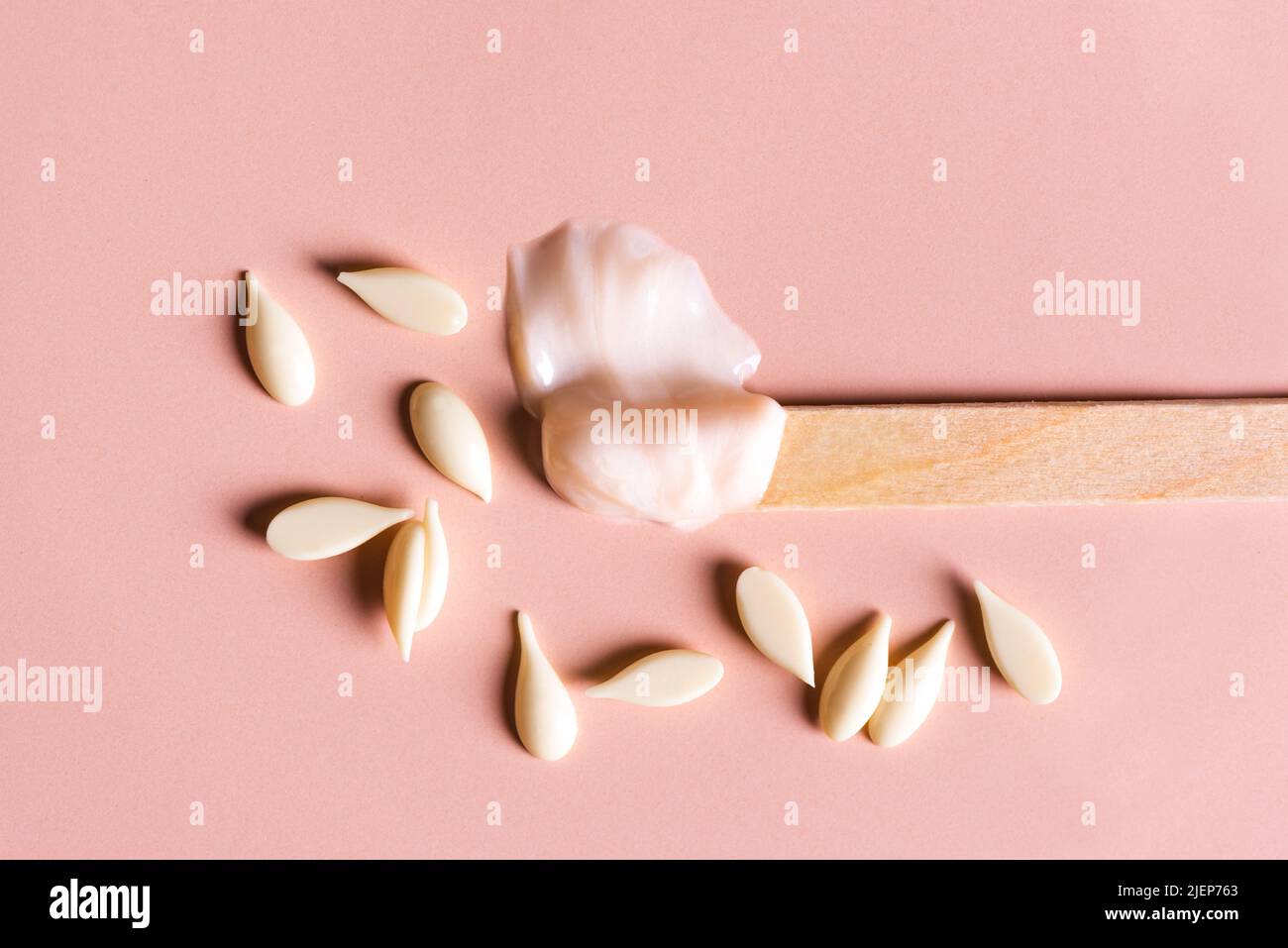 Melted and granular film wax beans and wooden spatula for depilation. Natural hair removal,  beauty concept, white  pearl wax on pink background, copy Stock Photo