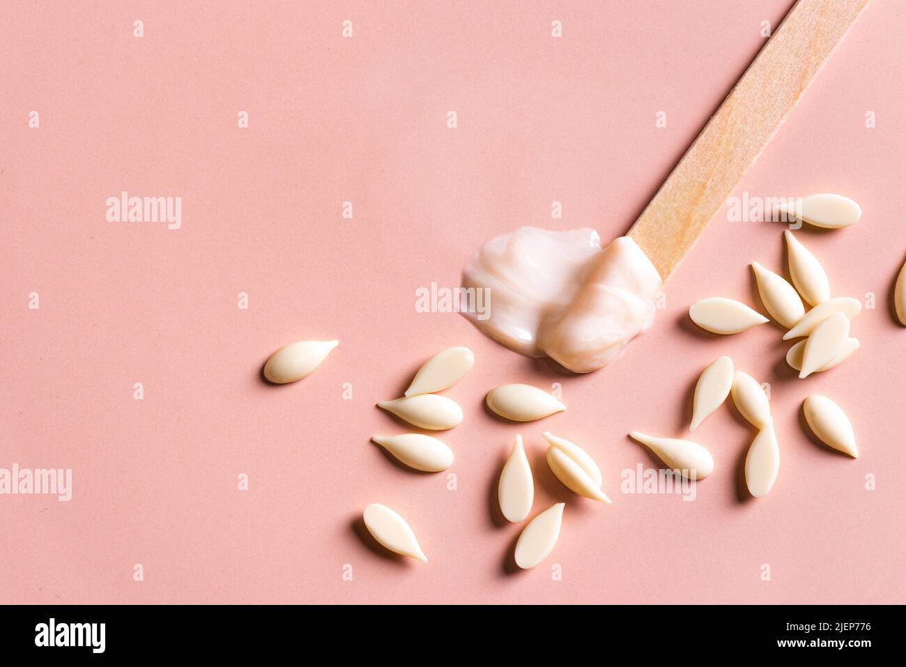 Melted and granular film wax beans and wooden spatula for depilation. Natural hair removal,  beauty concept, white  pearl wax on pink background, copy Stock Photo
