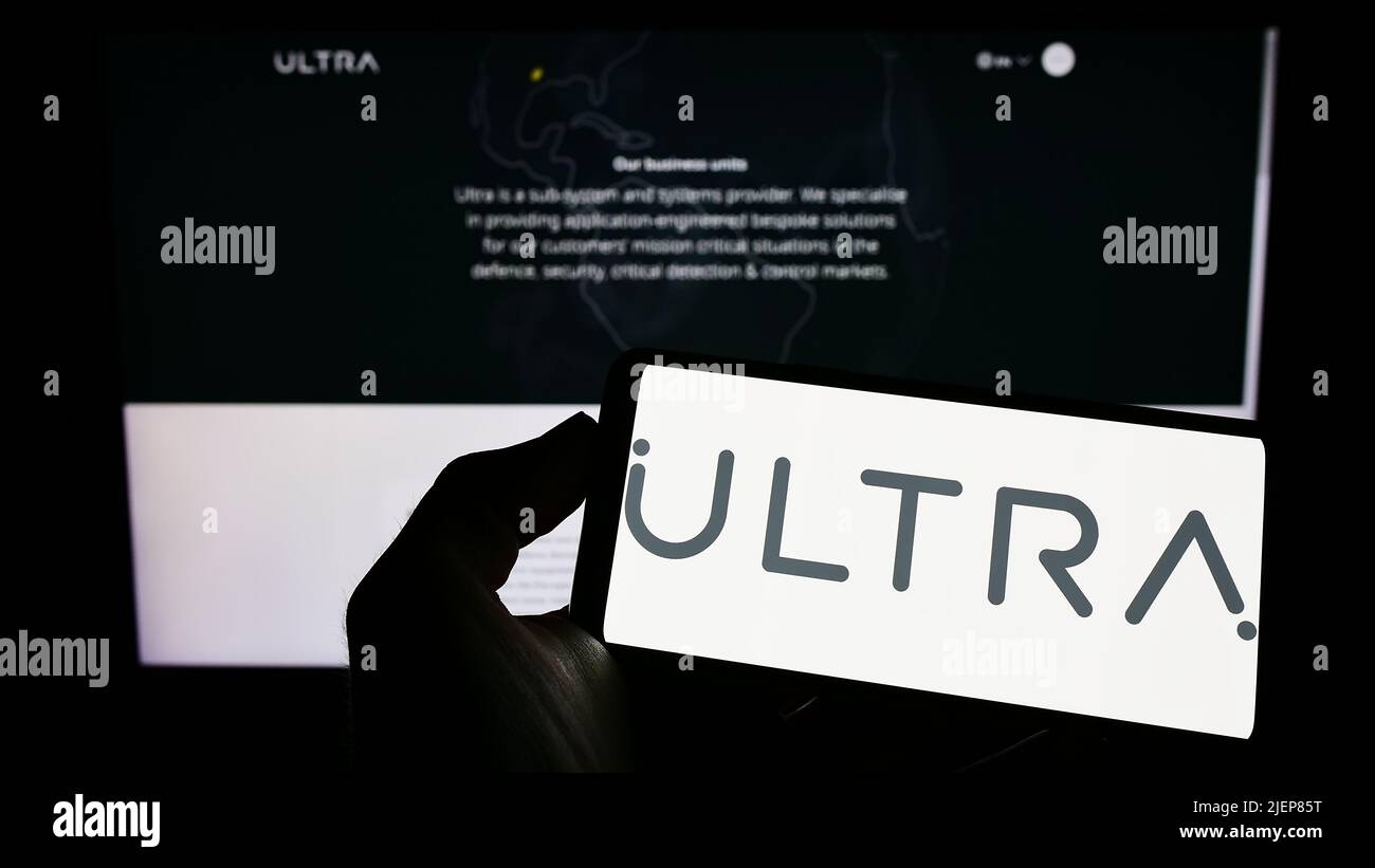 Person holding mobile phone with logo of British company Ultra Electronics Holdings plc on screen in front of web page. Focus on phone display. Stock Photo