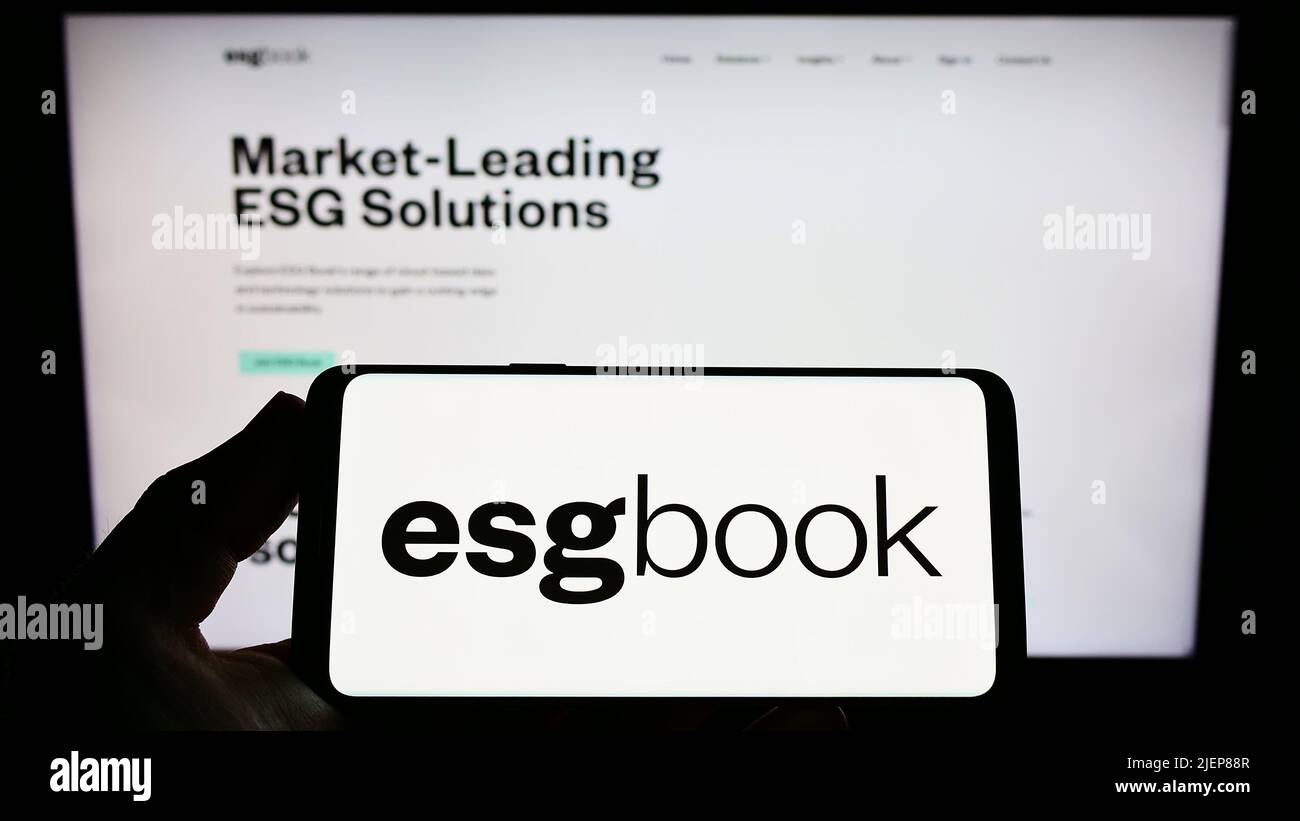 Person holding smartphone with logo of British sustainability data company ESG Book on screen in front of website. Focus on phone display. Stock Photo