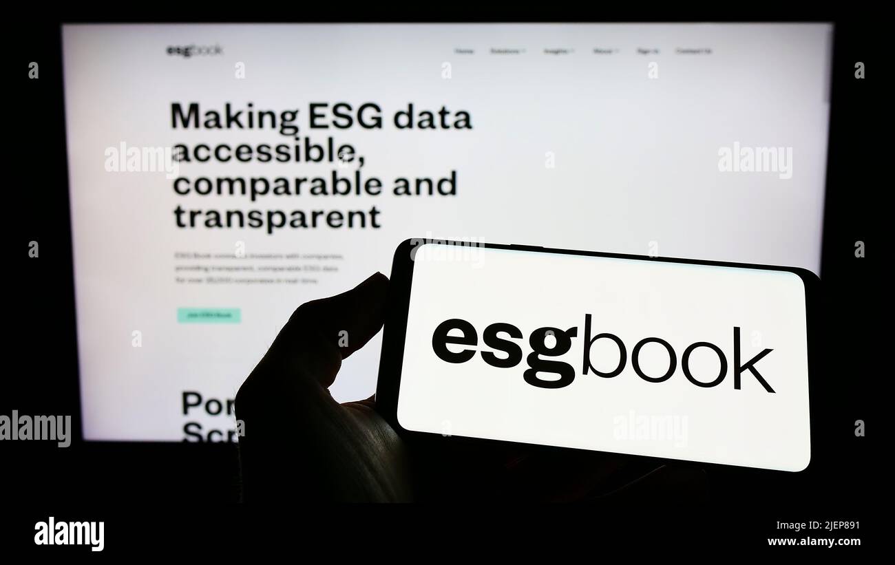 Person holding cellphone with logo of British sustainability data company ESG Book on screen in front of business webpage. Focus on phone display. Stock Photo