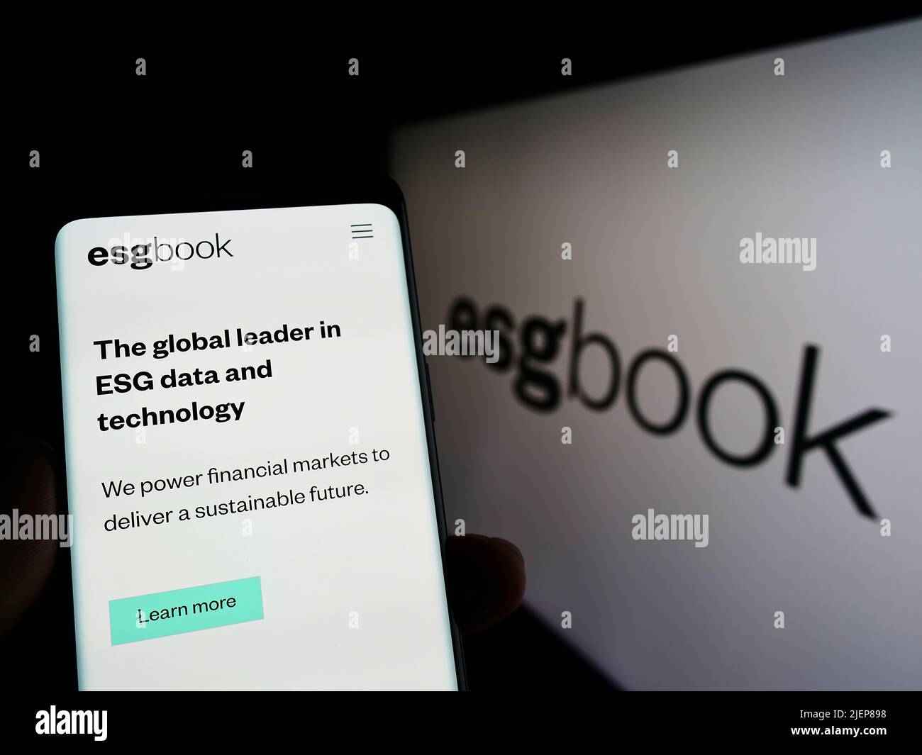 Person holding cellphone with webpage of British sustainability data company ESG Book on screen with logo. Focus on center of phone display. Stock Photo
