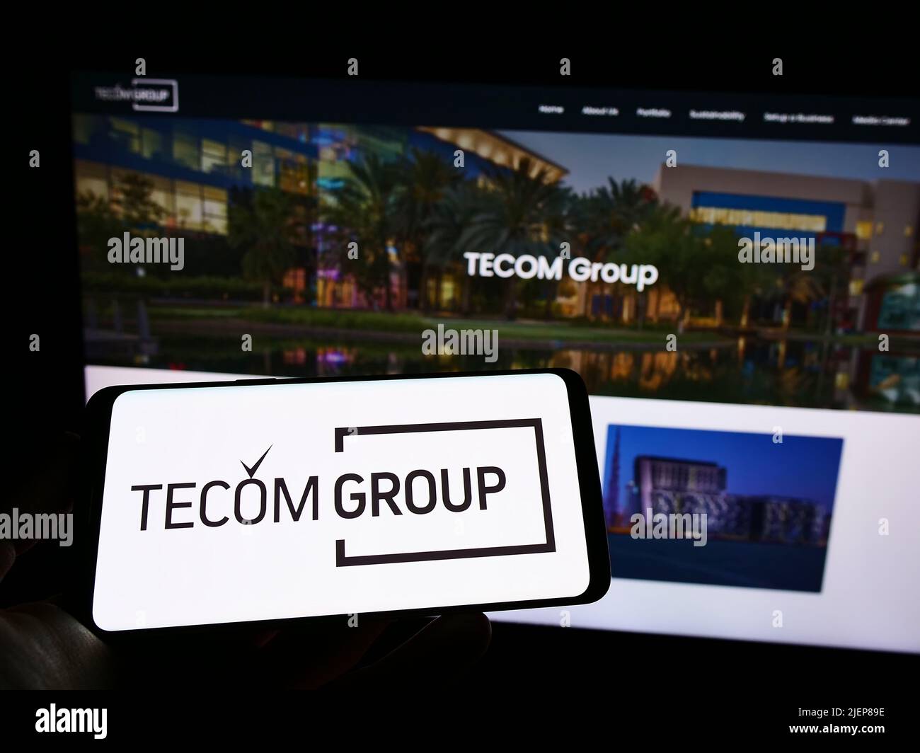 Person holding mobile phone with logo of Emirati real estate company Tecom Group LLC on screen in front of web page. Focus on phone display. Stock Photo