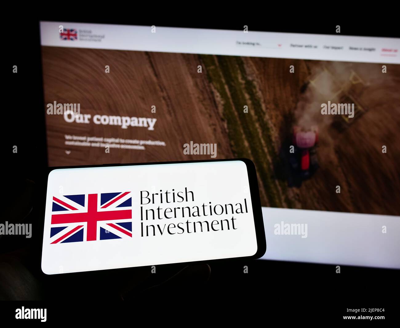 Person holding smartphone with logo of British International Investment (BII) on screen in front of website. Focus on phone display. Stock Photo