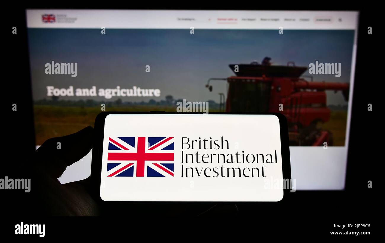 Person holding mobile phone with logo of British International Investment (BII) on screen in front of business web page. Focus on phone display. Stock Photo