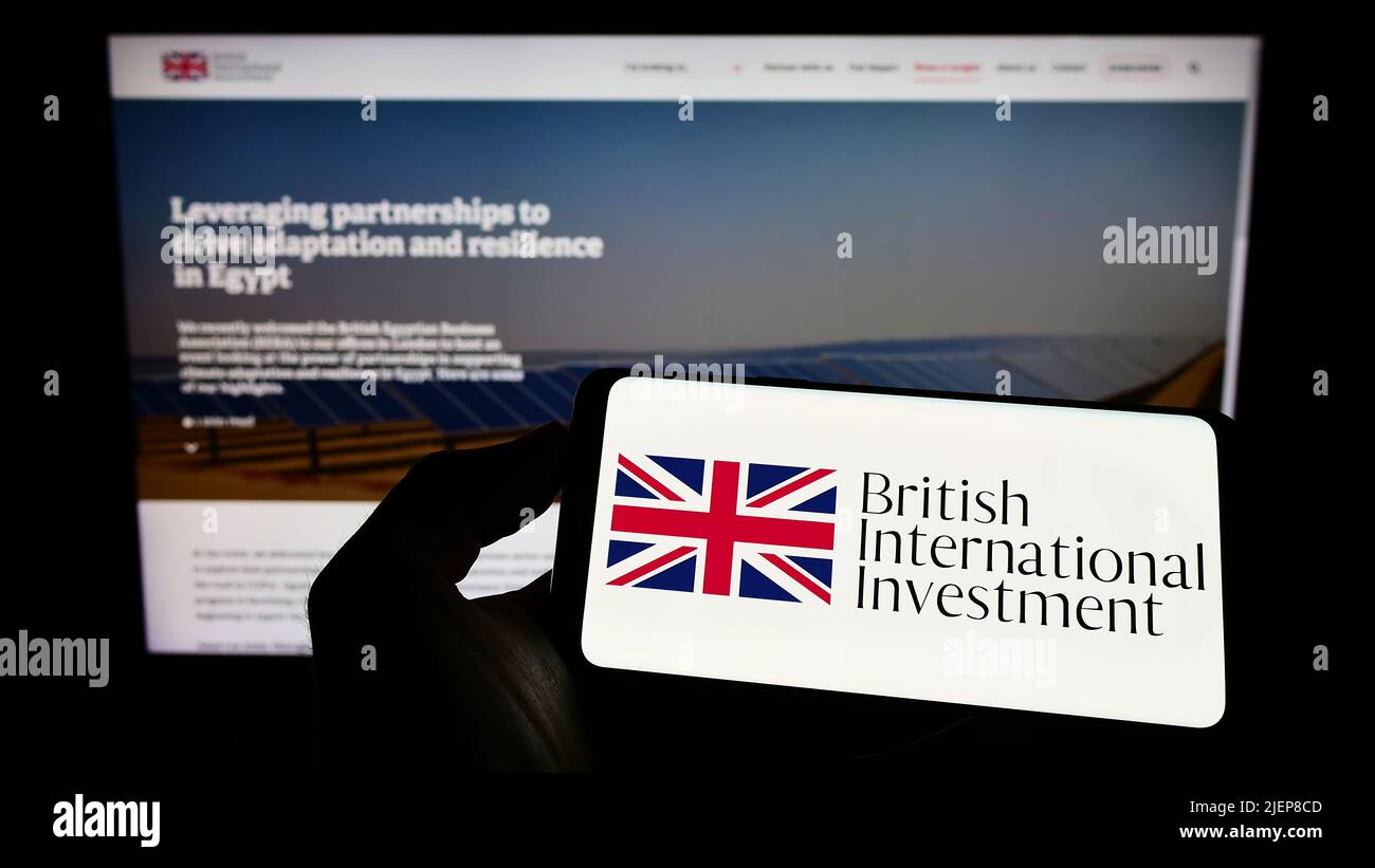 Person holding cellphone with logo of British International Investment (BII) on screen in front of business webpage. Focus on phone display. Stock Photo