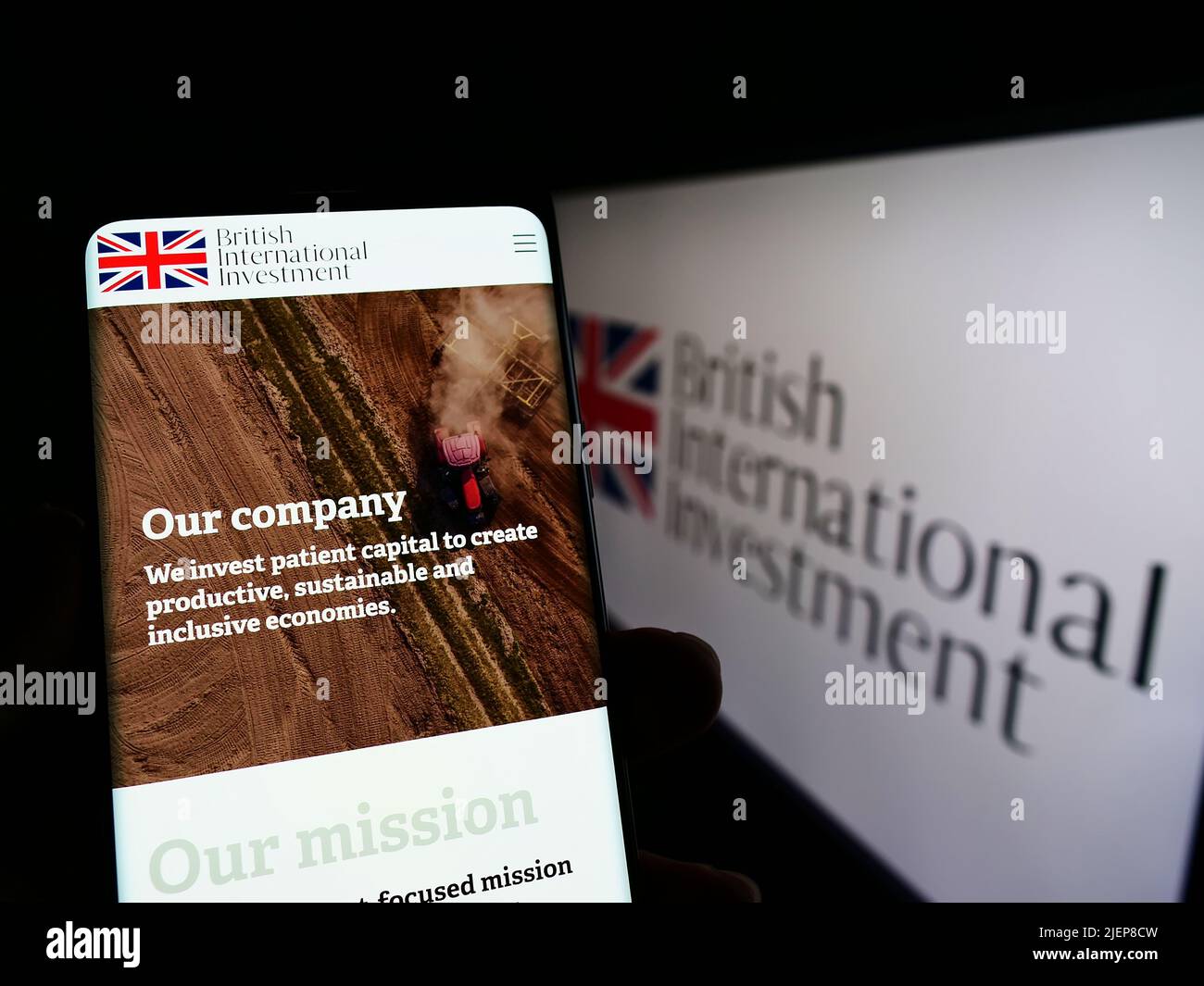Person holding mobile phone with webpage of British International Investment (BII) on screen in front of logo. Focus on center of phone display. Stock Photo