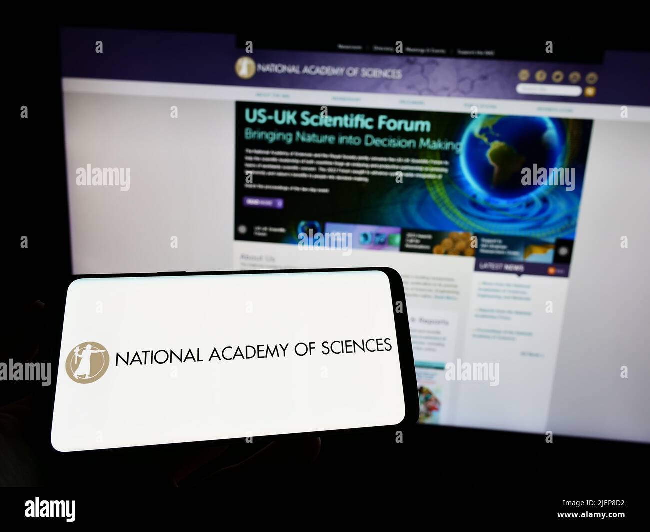 Person holding smartphone with logo of National Academy of Sciences (NAS) on screen in front of website. Focus on phone display. Stock Photo