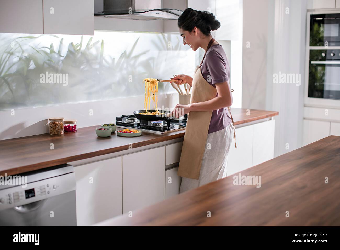 Side profile of a young woman cooking noodles in the kitchen Stock Photo