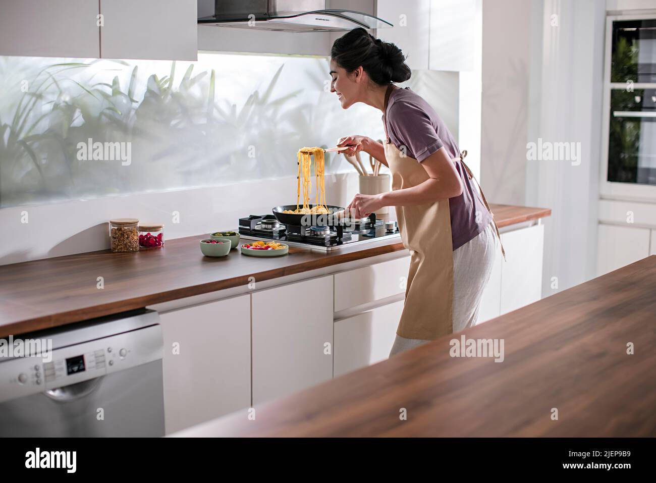 Side profile of a young woman cooking noodles in the kitchen Stock Photo
