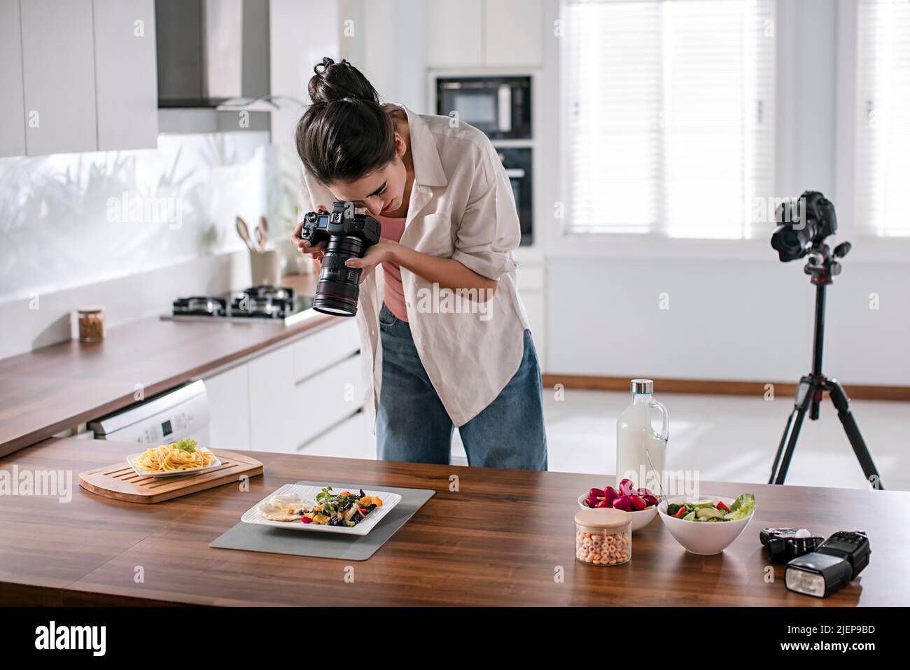 Young woman clicking pictures of food with a camera in the kitchen Stock Photo
