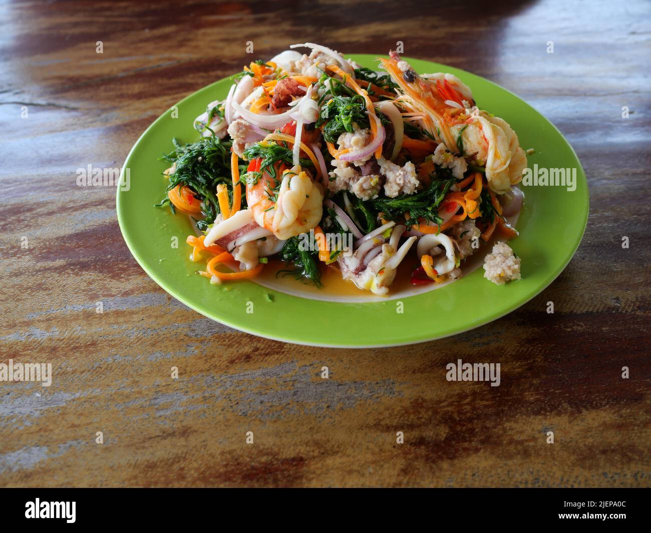 Thai cuisine spicy salad with Boiled Seablite ( Suaeda maritima ) leaf with squid and shrimp in green dish on brown wooden table, Seafood in Thailand Stock Photo