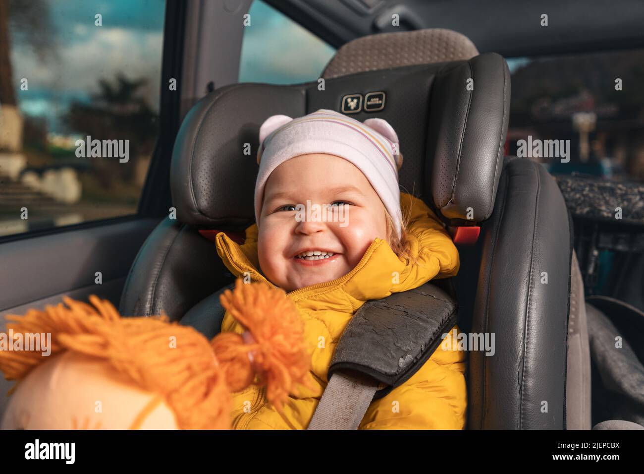 Portrait of a happy little kid sitting in a child seat in the back seat