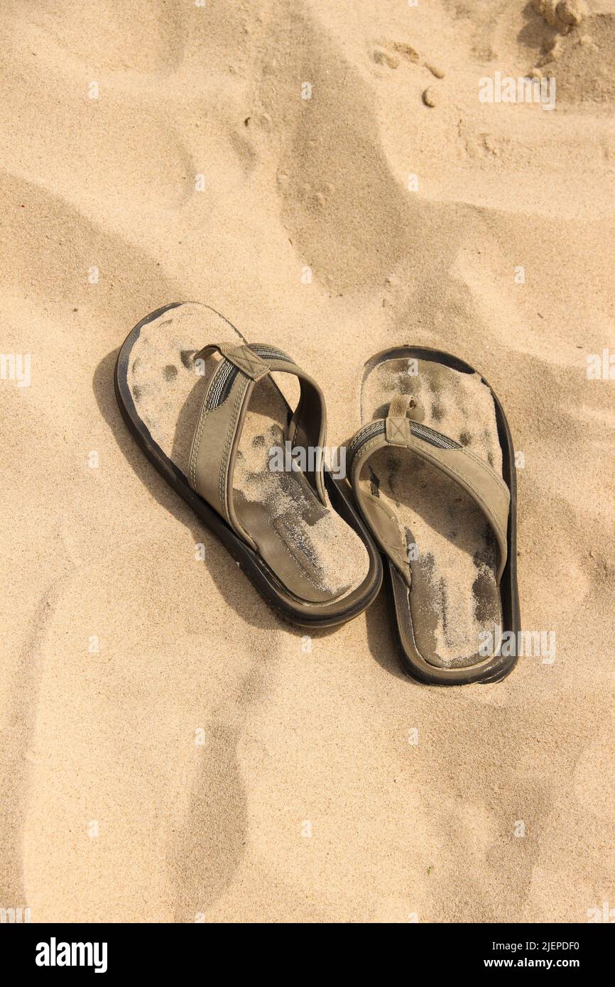 Comfy flip-flops lay on the sand. Summer footwear dropped at the beach. Stock Photo