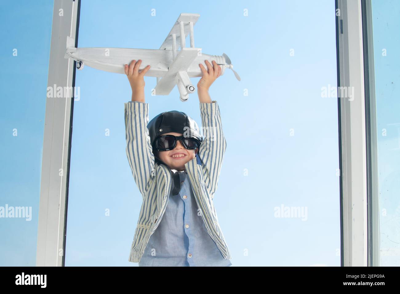 Child boy with pilot goggles and helmet playing with wooden toy