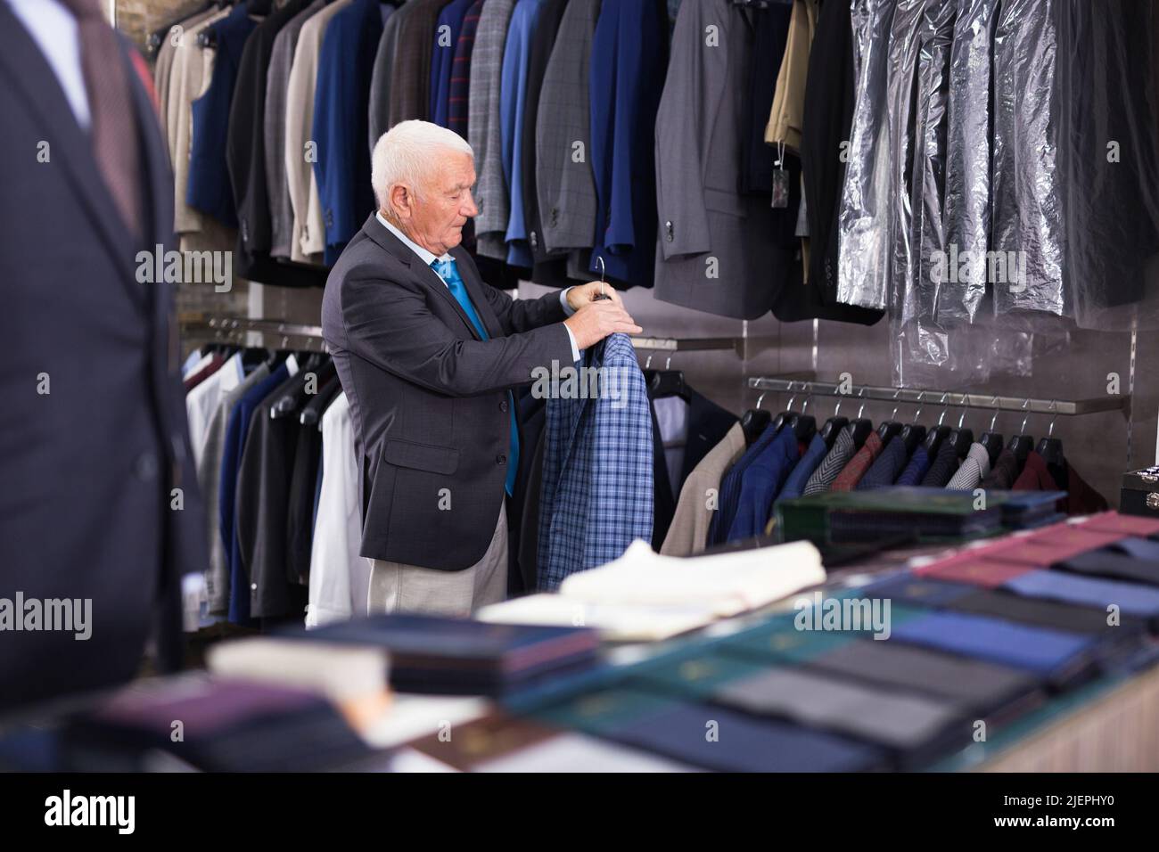 Elderly male shopper choosing fashionable blazer in clothing store