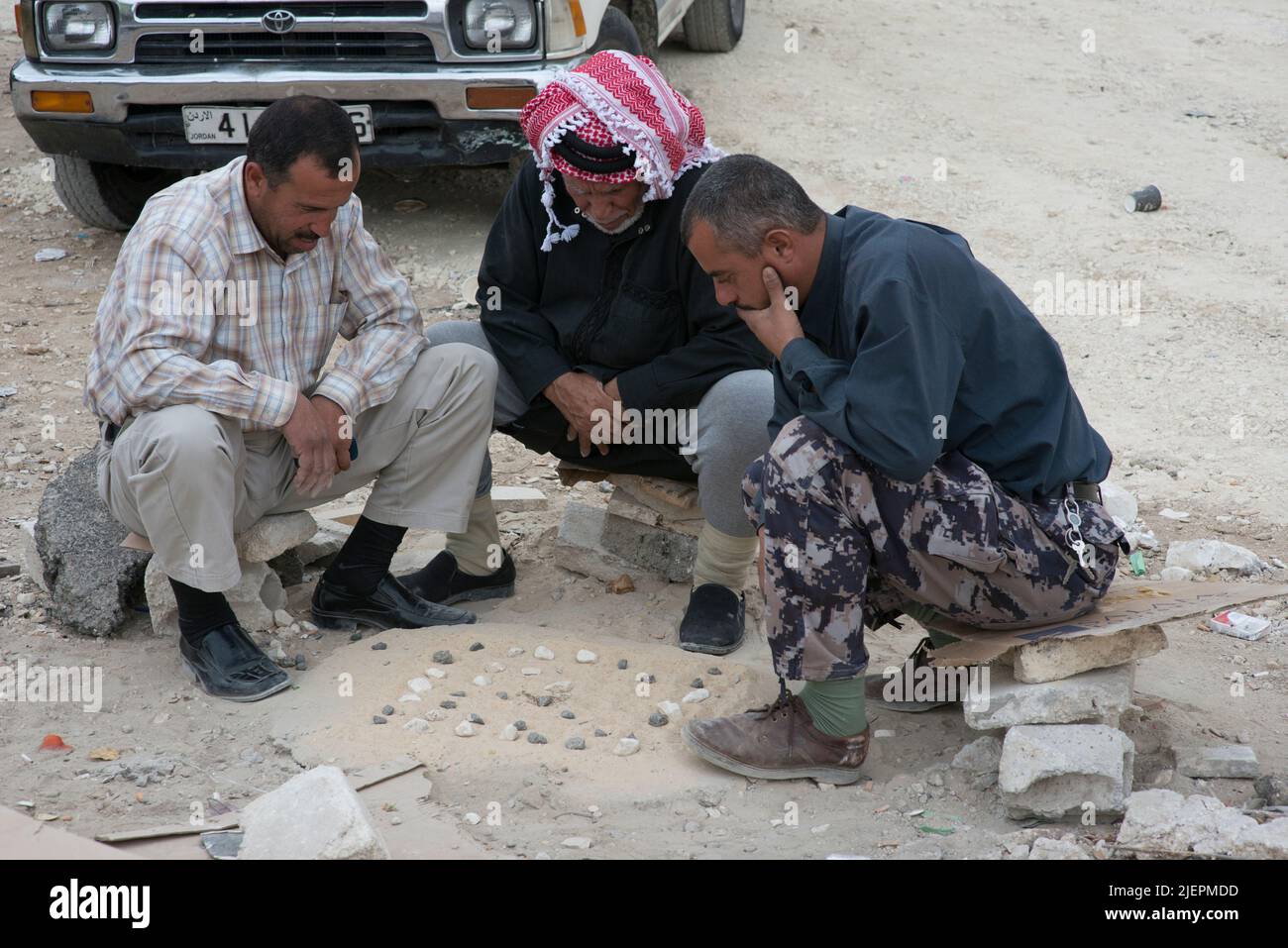 Amman, Jordan. Three Arabic men sitting in de urban, dessert sand killing  using their free time to pay a board game using the sand floor and found stones. Stock Photo