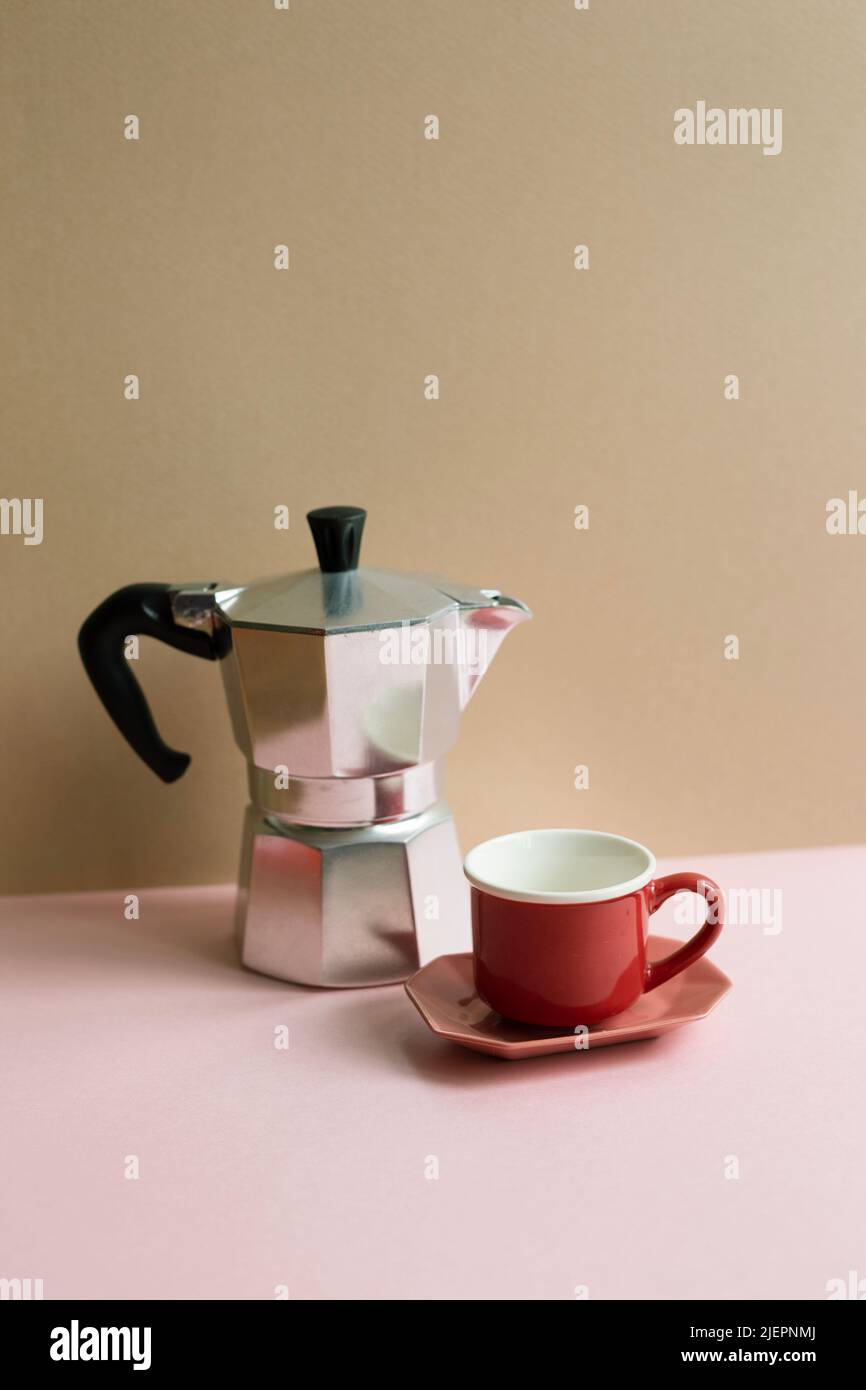 Italian coffee maker mocha coffee pot and cup on pink table. beige wall background Stock Photo