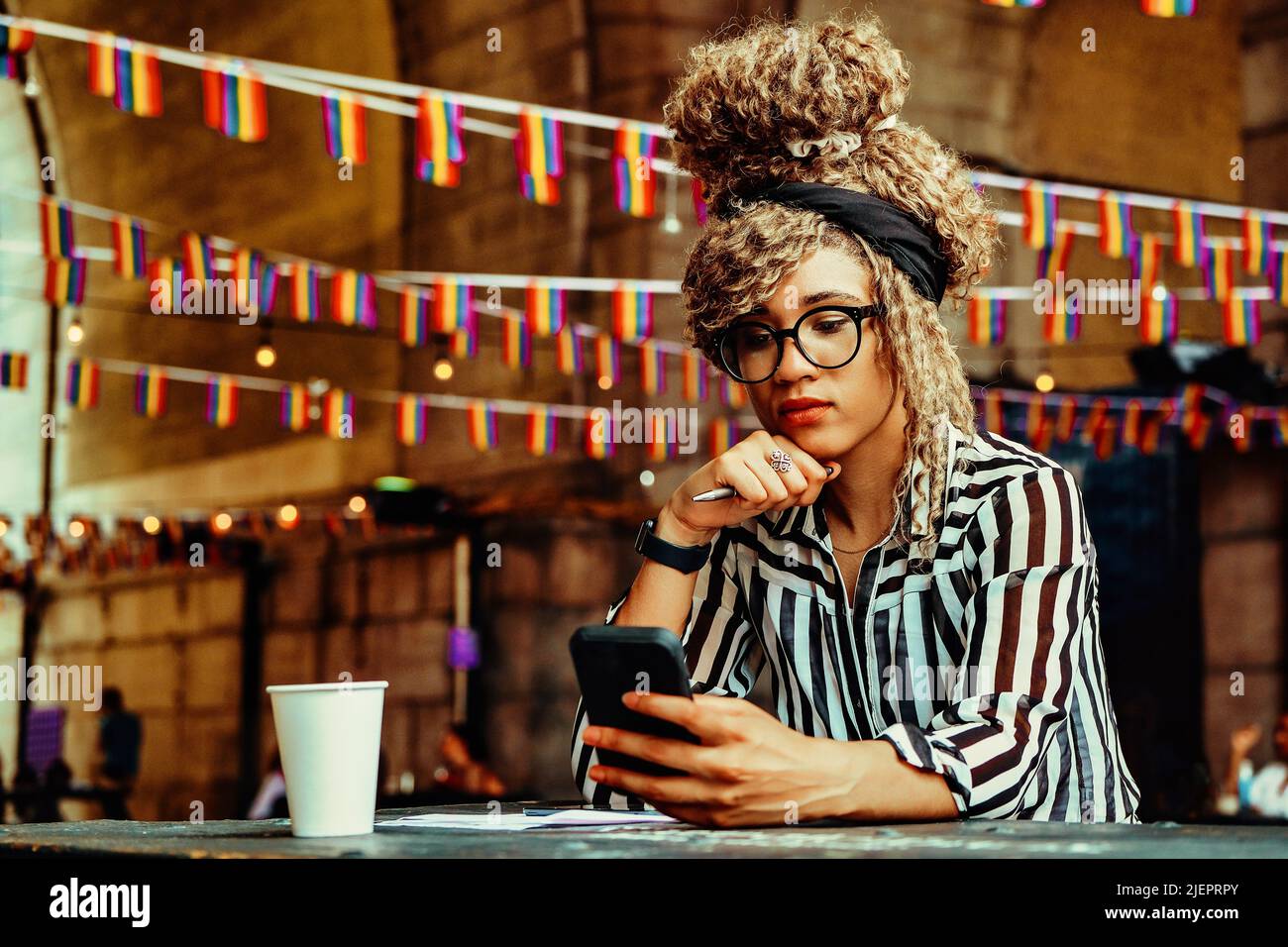 Portrait of serious woman with afro hairstyle reading news on smartphone sitting in a coffeehouse shot Stock Photo