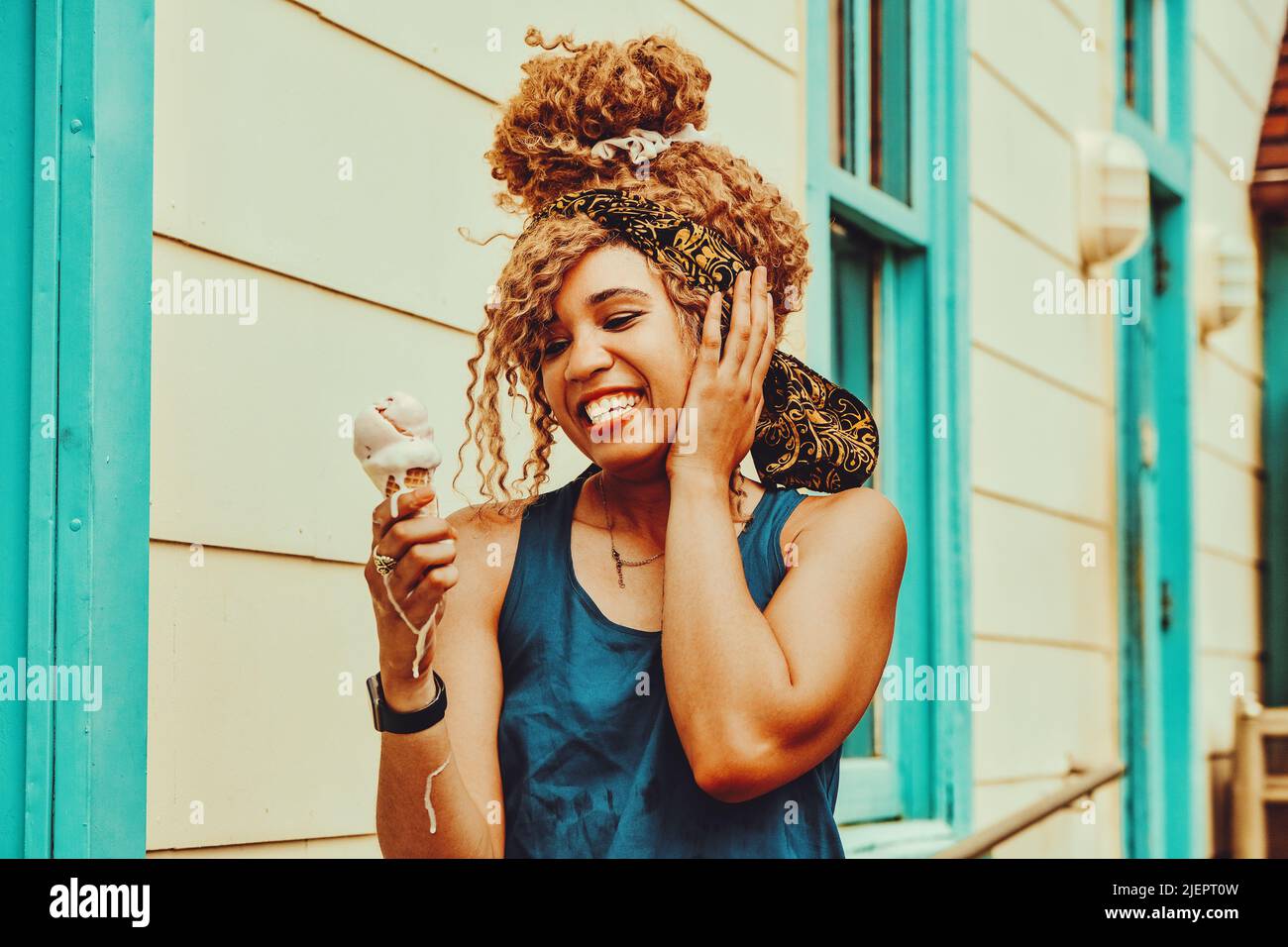 young adult woman afro hair smiling eating ice cream outdoors summertime looking away shot Stock Photo