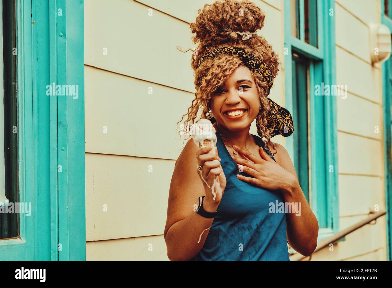 young adult woman afro hair smiling eating ice cream outdoors summertime looking at camera shot Stock Photo