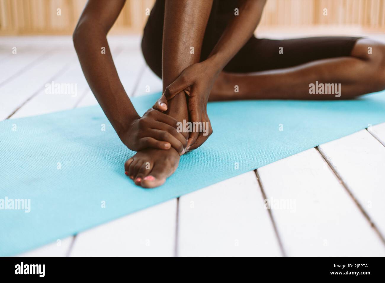 Unrecognizable barefoot dark skin multiracial woman touching feet. Stretch and do yoga. Stiff foot tendons, ligaments  Stock Photo
