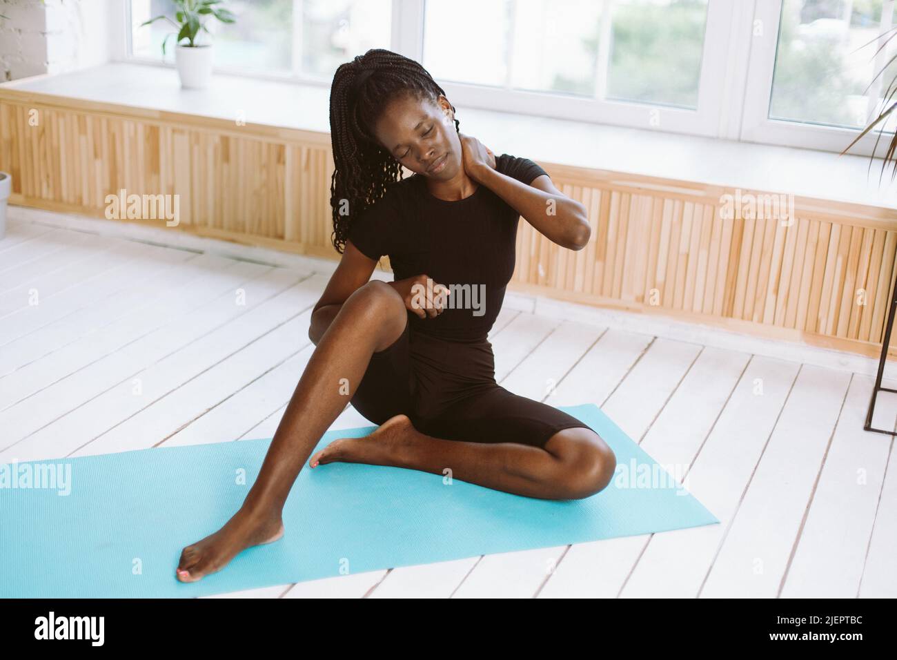 Portrait dark skin multiracial woman with dreadlocks stretch, do yoga exercises on mat in gym. Rubbing body. Health care Stock Photo