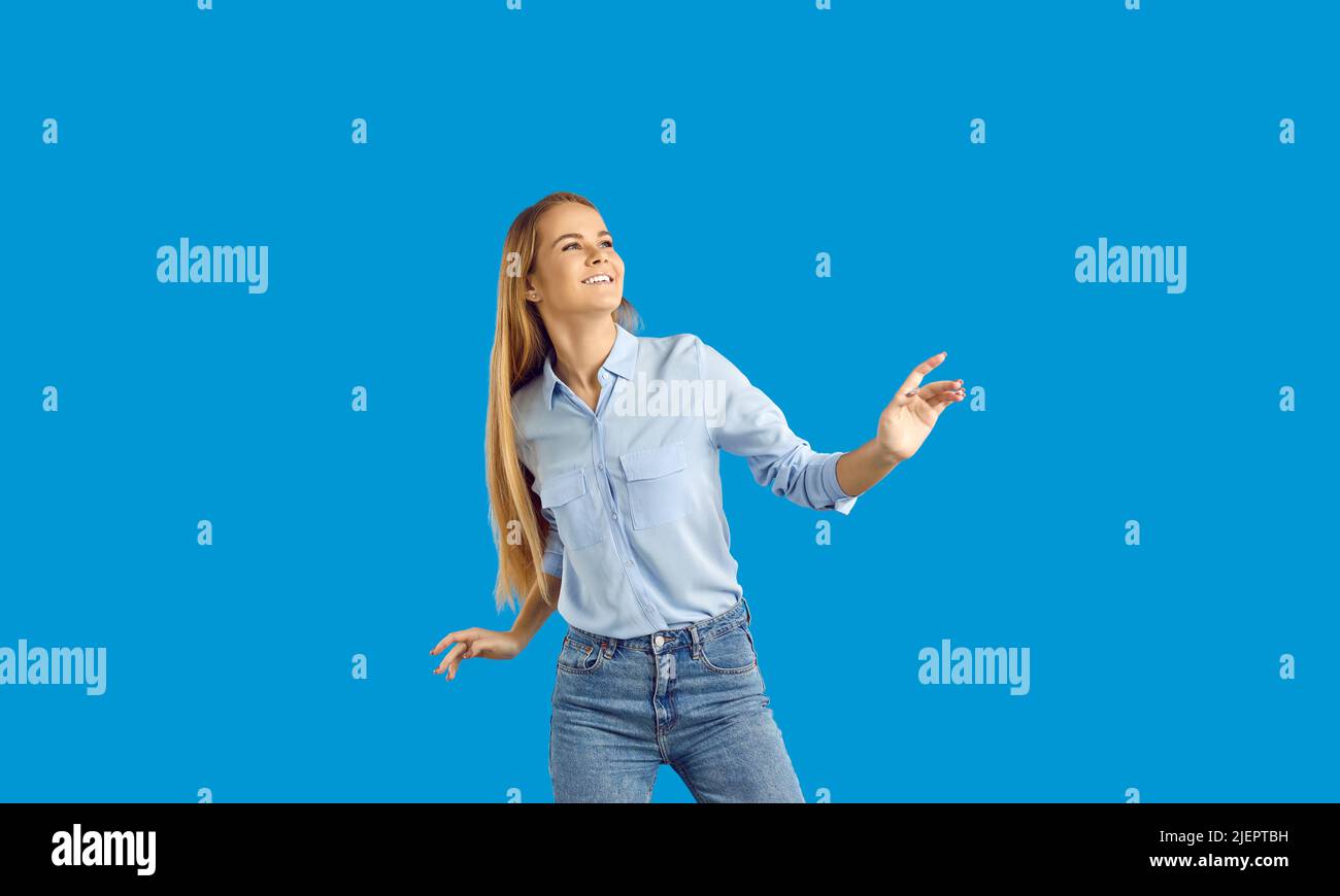 Happy and relaxed, carefree caucasian blond girl having fun, listening music vibing, raise hands up and dancing joyful, smiling and standing blue Stock Photo