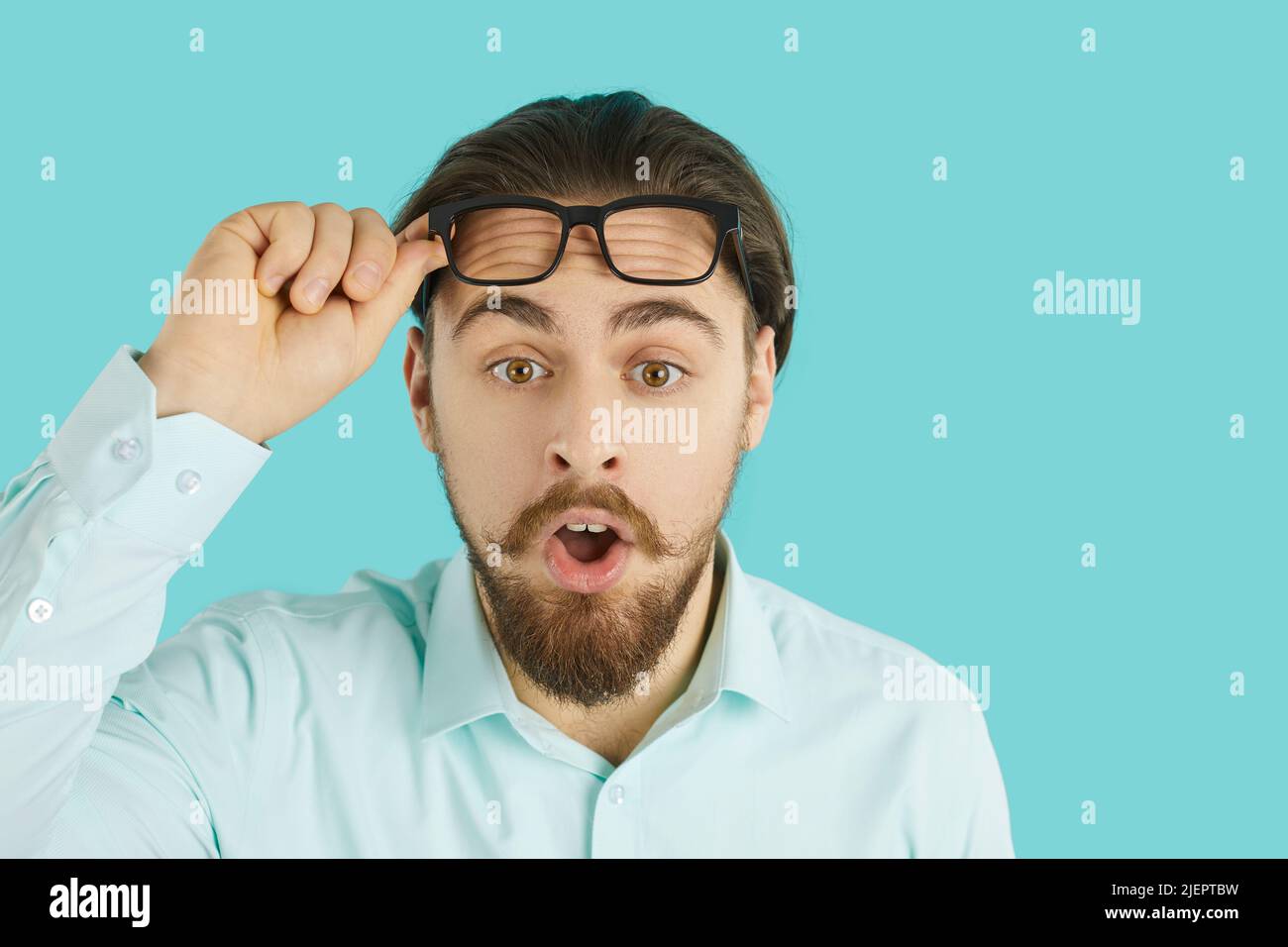 Young man lifts his glasses and looks at something with funny astonished face expression Stock Photo