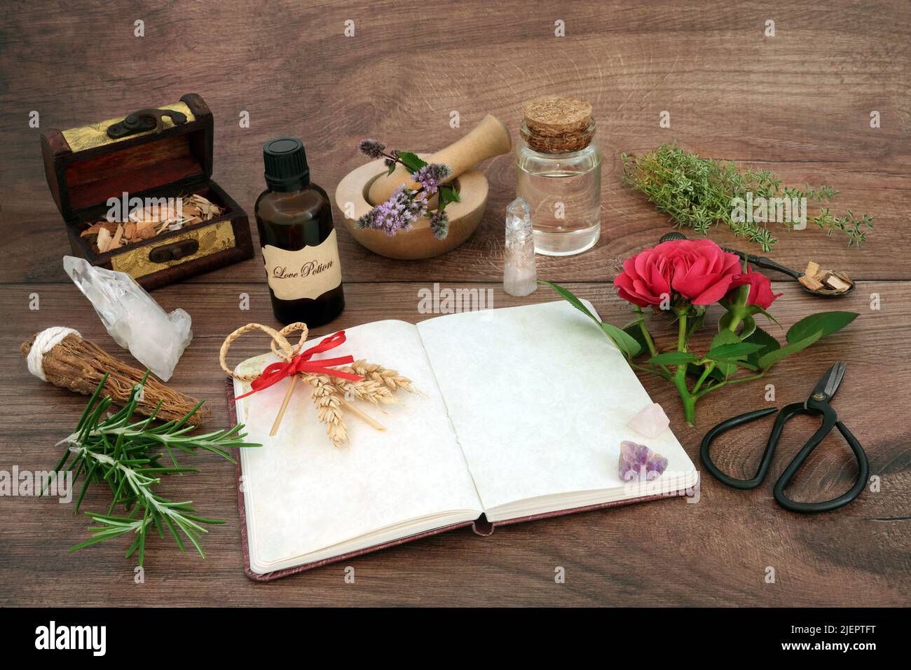 Love potion preparation with recipe notebook, corn dolly for fertility occult ritual, rose flower, herbs, crystals, oil and honey for magic spells. Stock Photo