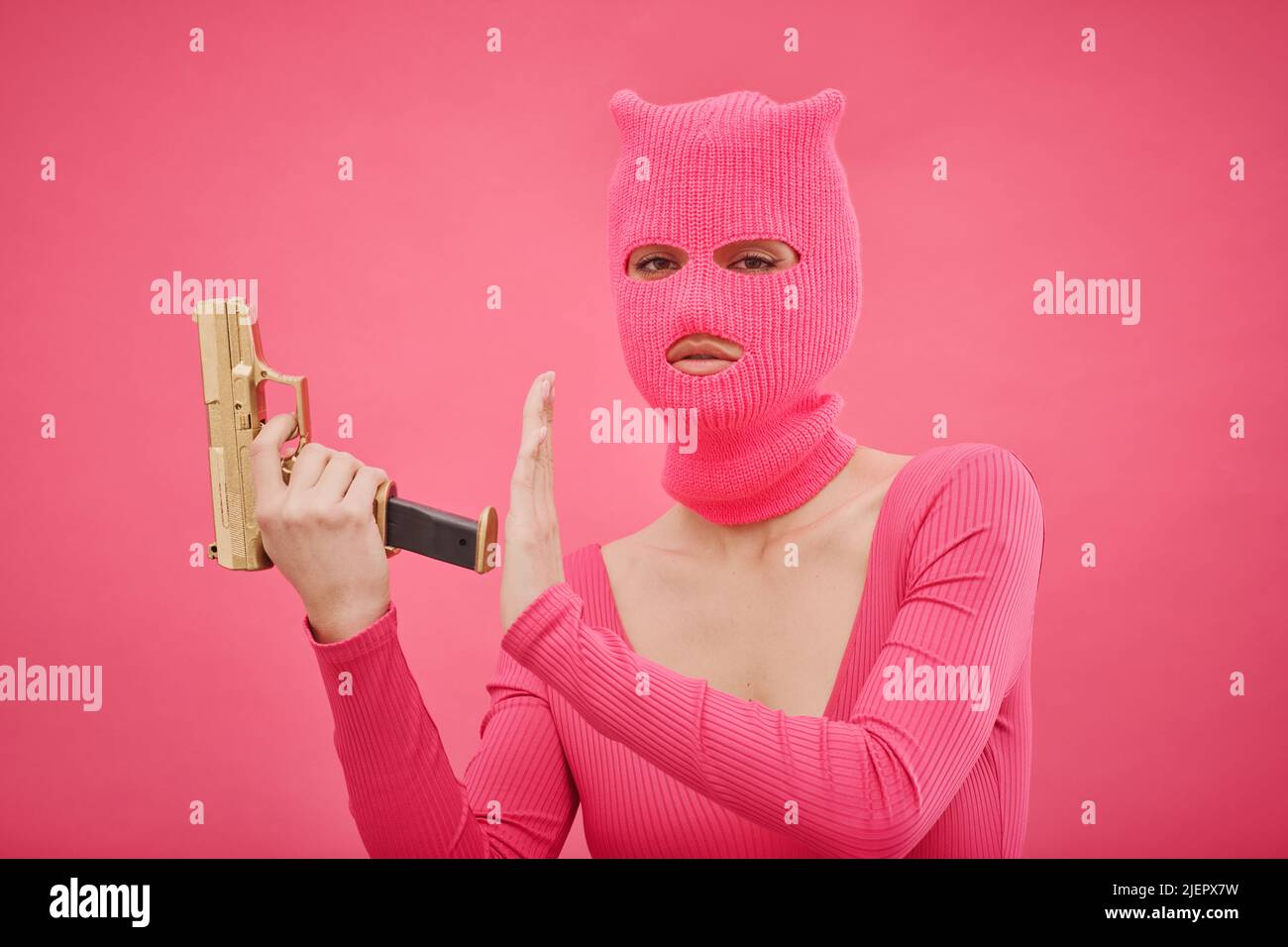 Portrait of criminal girl in pink balaclava holding gun and looking at