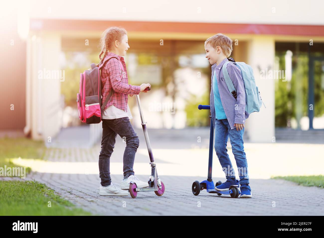 Girl and boy standing with scooters at school and talking together. Stock Photo