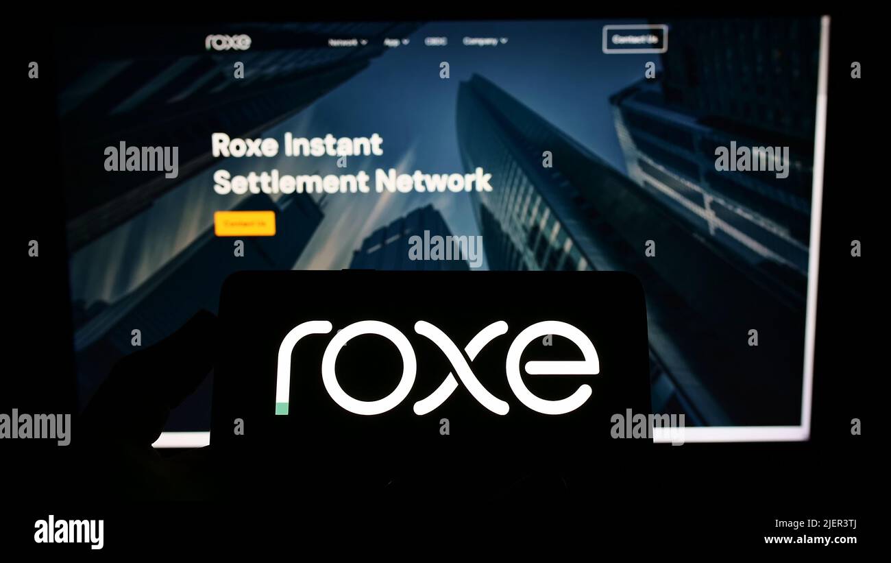 Person holding smartphone with logo of US blockchain company Roxe Holding Inc. on screen in front of website. Focus on phone display. Stock Photo