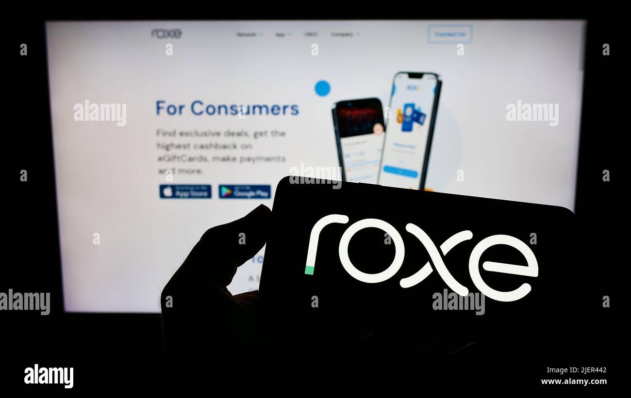 Person holding smartphone with logo of American blockchain company Roxe Holding Inc. on screen in front of web page. Focus on phone display. Stock Photo