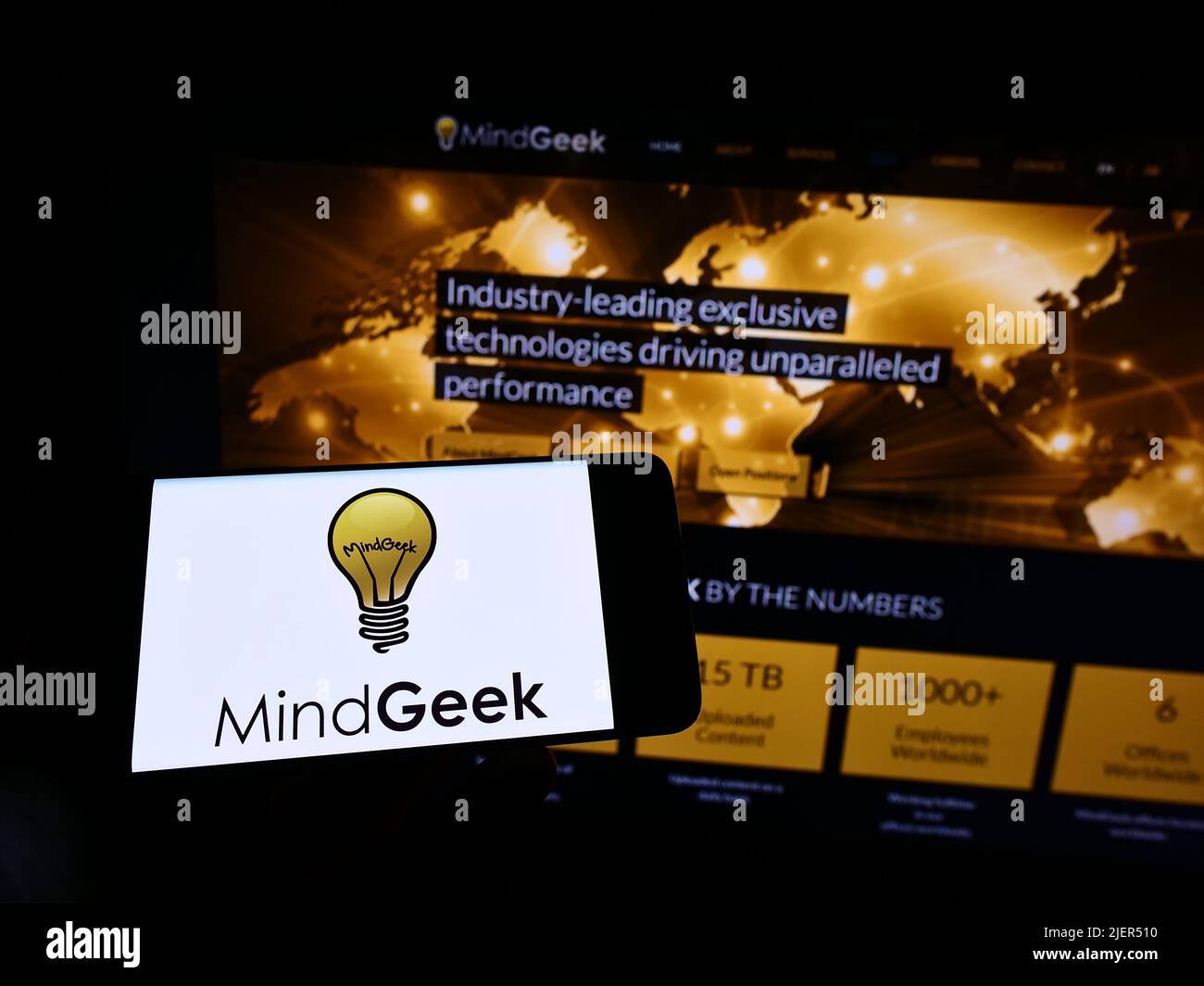 Person holding mobile phone with logo of pornography company MindGeek SARL on screen in front of business web page. Focus on phone display. Stock Photo