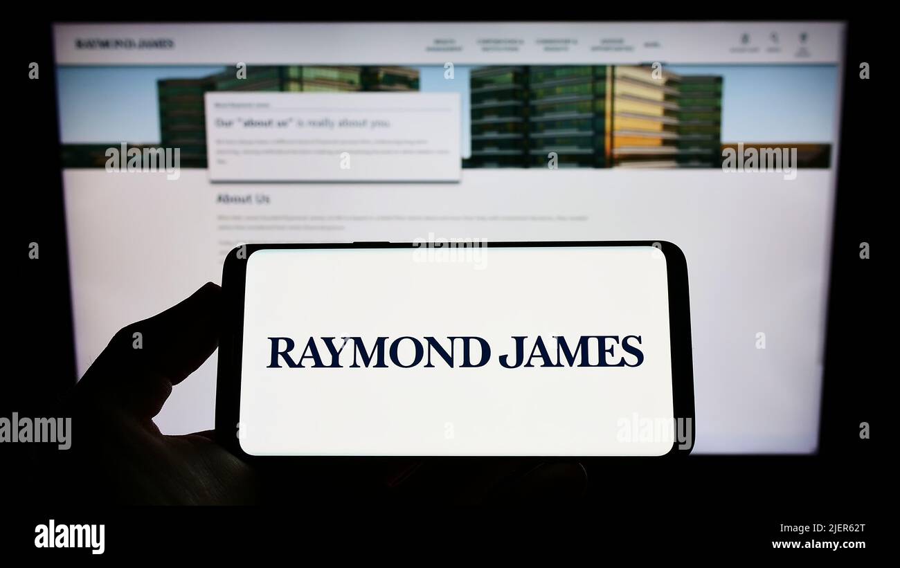 Person holding smartphone with logo of US company Raymond James Financial Inc. on screen in front of website. Focus on phone display. Stock Photo