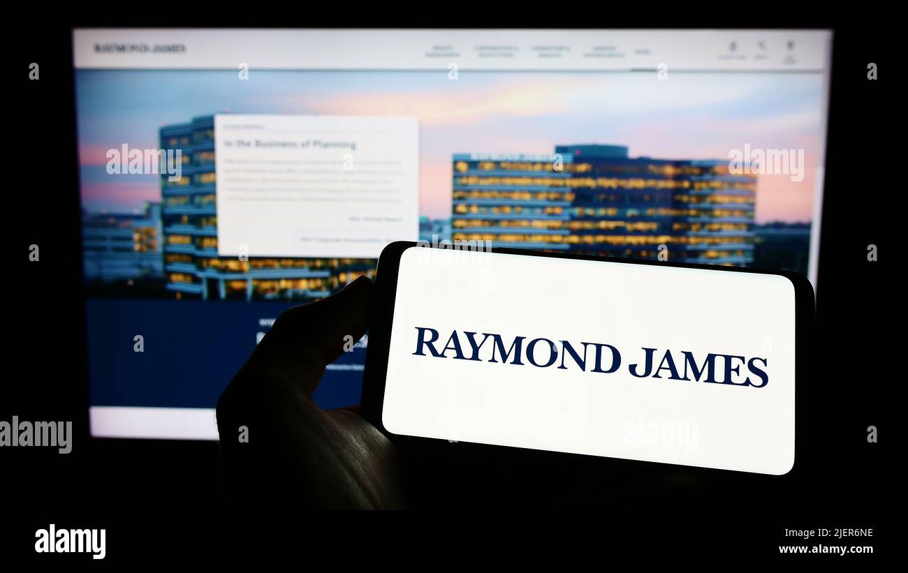 Person holding cellphone with logo of US company Raymond James Financial Inc. on screen in front of business webpage. Focus on phone display. Stock Photo