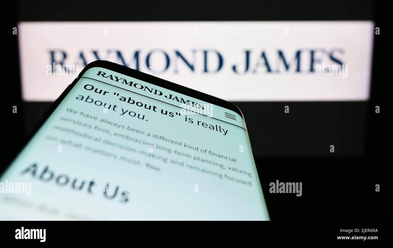 Mobile phone with website of US company Raymond James Financial Inc. on screen in front of business logo. Focus on top-left of phone display. Stock Photo