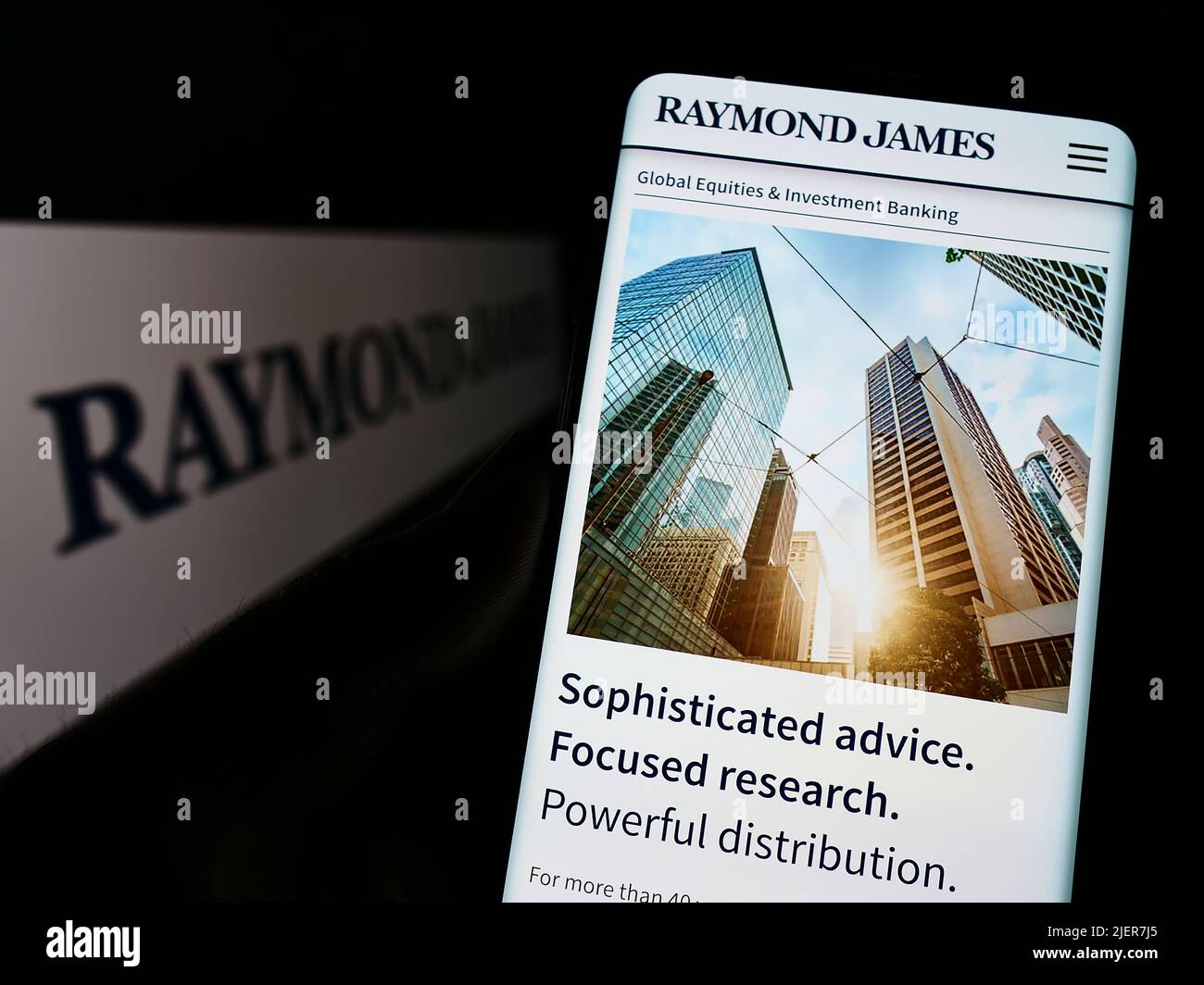 Person holding cellphone with webpage of US company Raymond James Financial Inc. on screen in front of logo. Focus on center of phone display. Stock Photo