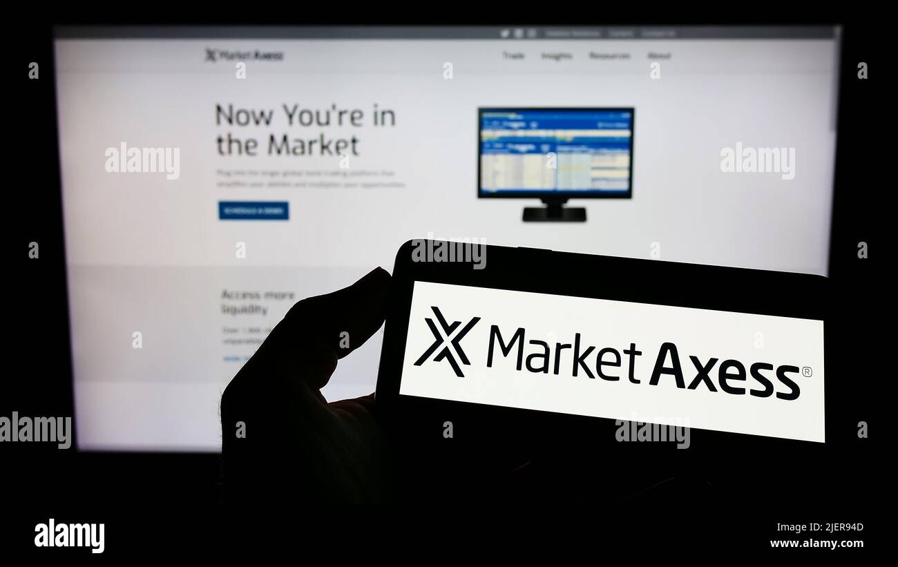 Person holding mobile phone with logo of US financial company MarketAxess Holdings Inc. on screen in front of web page. Focus on phone display. Stock Photo