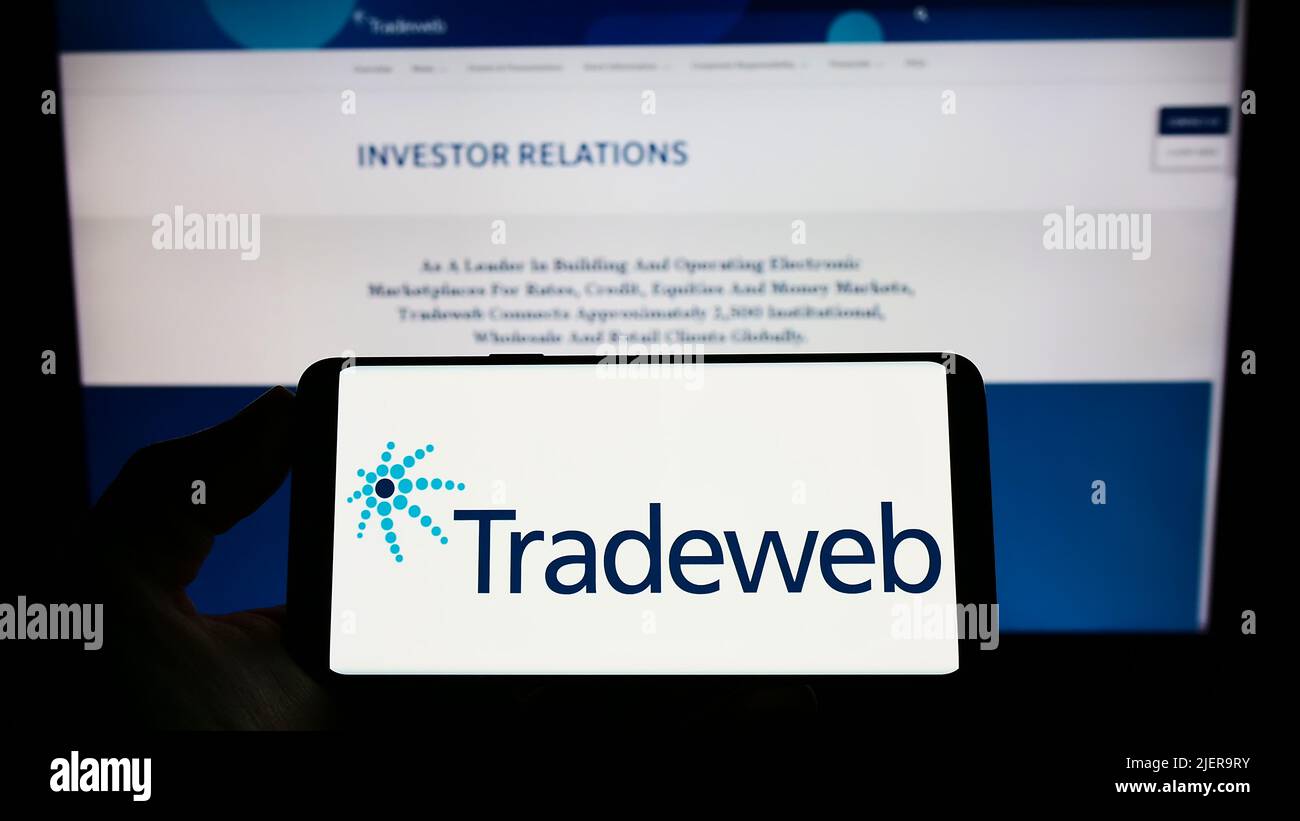 Person holding smartphone with logo of US financial company Tradeweb Markets Inc. on screen in front of website. Focus on phone display. Stock Photo