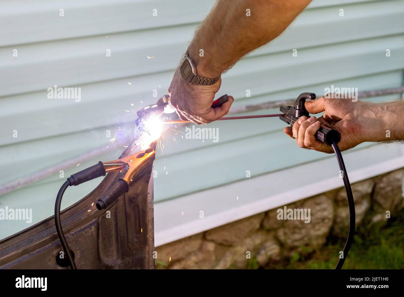 The hands of a man hold a welding machine and are engaged in welding ...