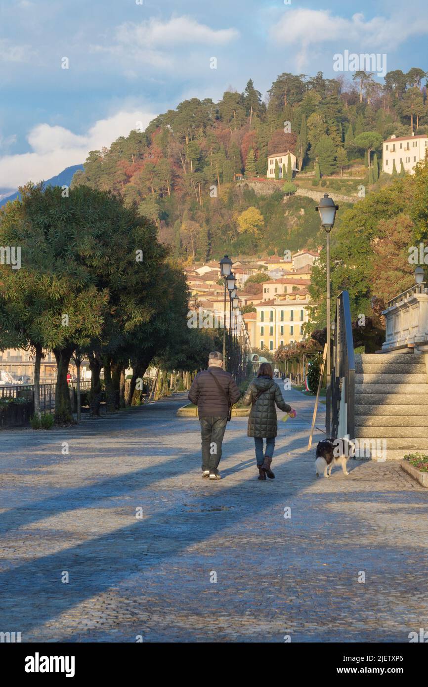 Bellagio, Italy, November 2021. A man and a woman walk their dog along the Bellagio promenade on the shores of Lake Como. Walks along the lake. Journe Stock Photo