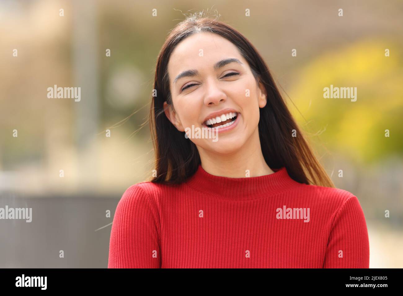 Front view portait of a happy woman in red laughing at camera in a park Stock Photo