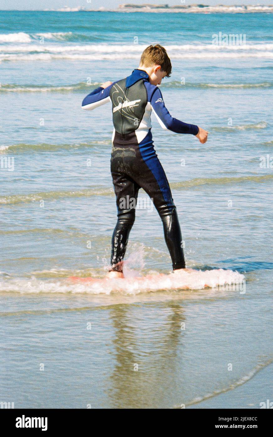 Twelve year old boy skimboarding at West Wittering beach, West Sussex