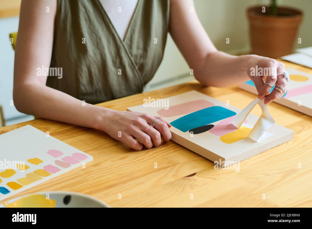 Hands of young creative female sitting by wooden table in workshop or studio and using stencil while creating new abstract painting Stock Photo