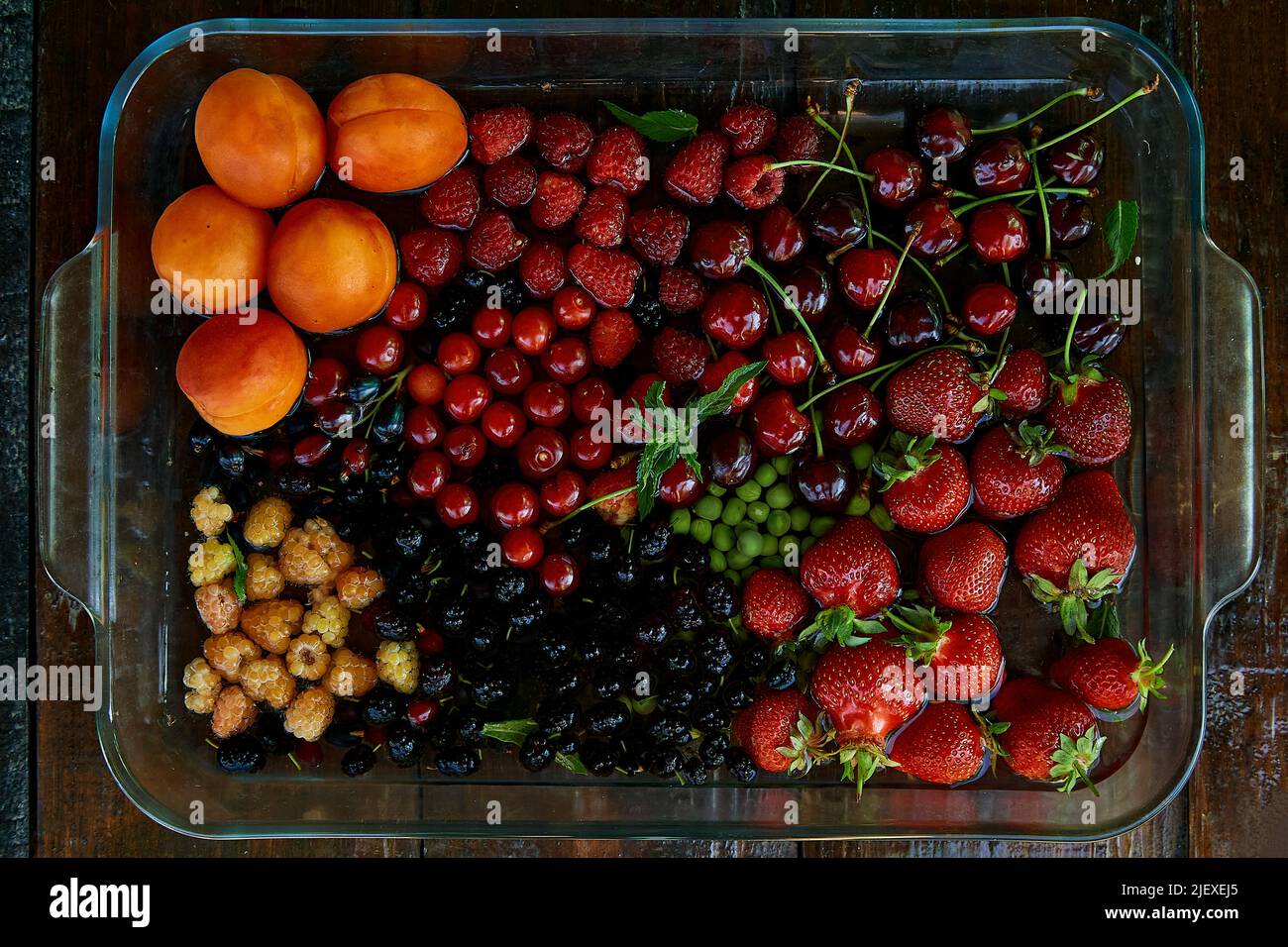 Assorty of fresh seasonal fruits and berries: strawberries, apricots, cherries, mulberry, raspberry washing under natural light. Healthy food, natural dessert, organic food. Stock Photo