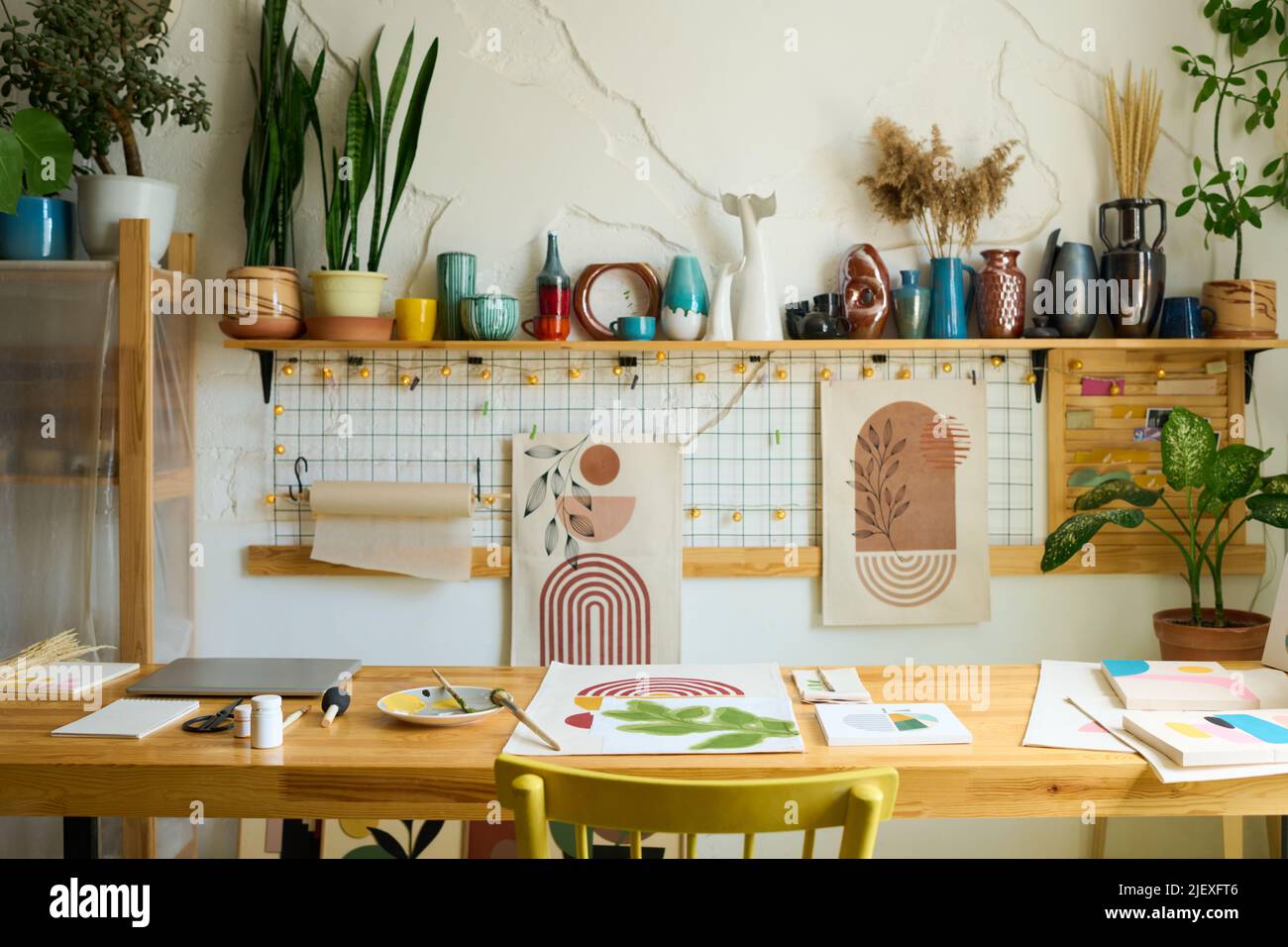 Interior of workshop of contemporary designer or studio of artist with supplies for painting on table and handmade items on shelf along wall Stock Photo